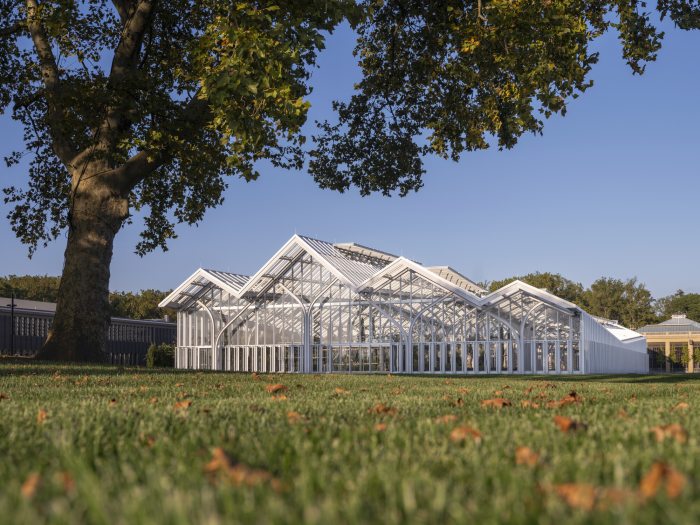A large glass conservatory photographed from the distance, featuring peaked roofs and white steel.