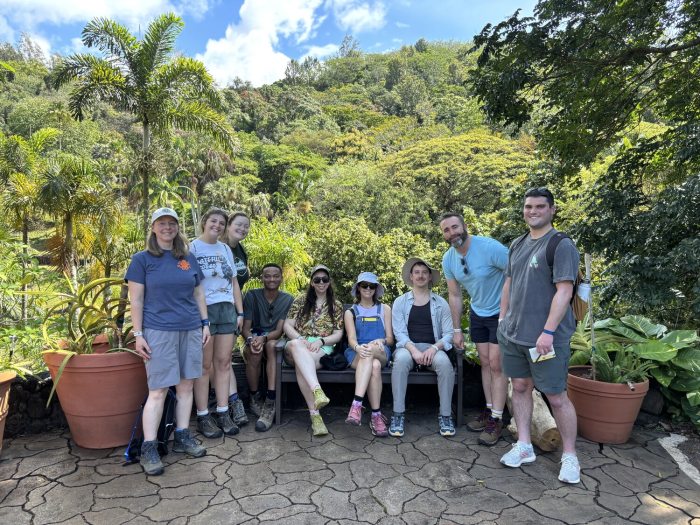 A group of people standing shoulder to shoulder in front of a tropical mountain range.