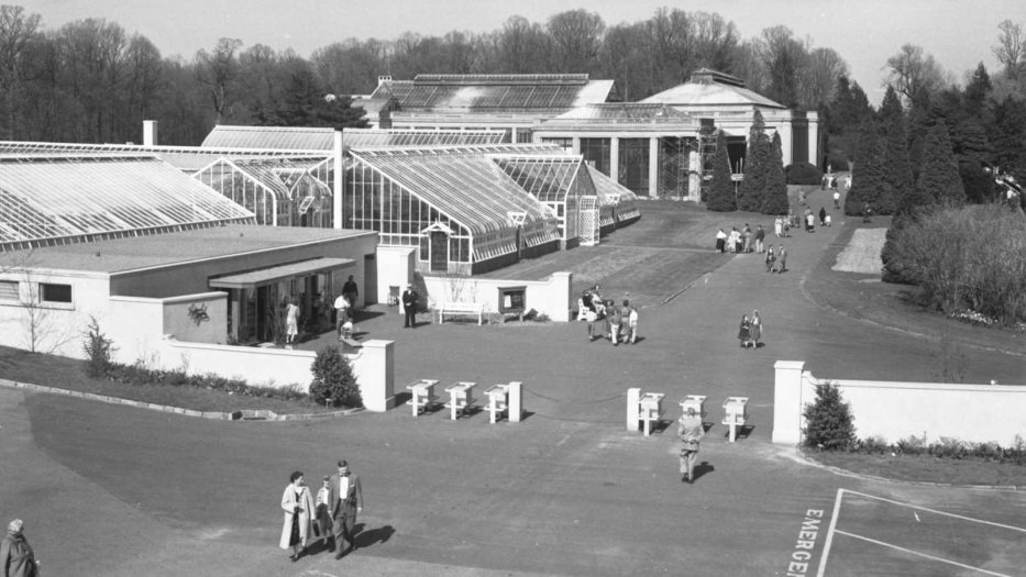 b&w image of people entering garden grounds and large Conservatory greenhouses
