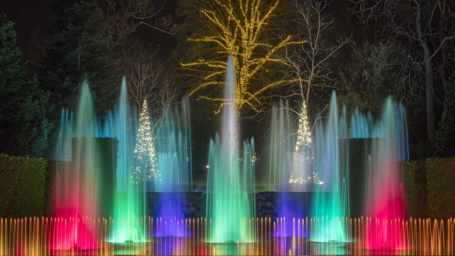 colorful fountains shoot in the air surrounded by decorated Christmas trees