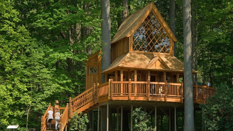 a brown treehouse with windows set in a wooded area