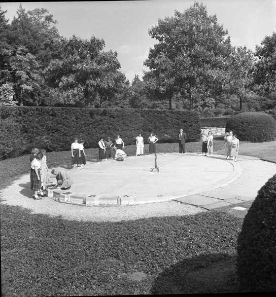 Students stand around a stone oval sundial on the ground in black and white photo