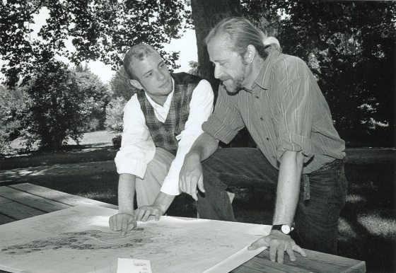 Two men stand looking over a map laid out on a table