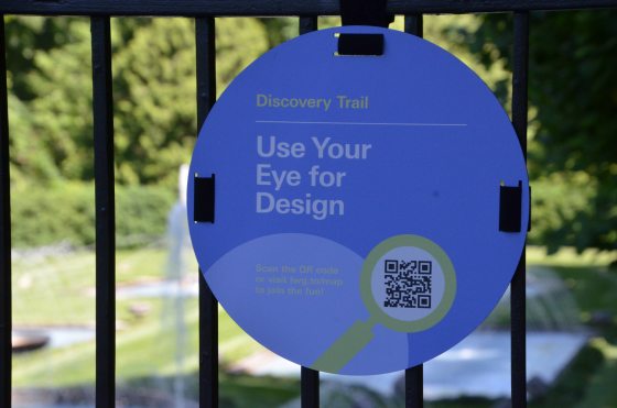A small blue circular sign is attached to a metal fence and displays a QR code