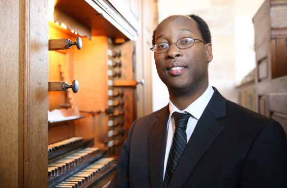 kola owolabi facing the camera next to an organ console