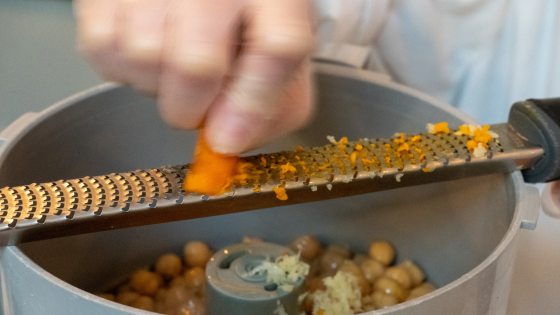 close up of person grating turmeric over a bowl of chickpeas