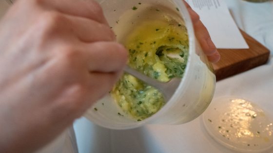 person's hand mixing up garlic and herb butter in  a white cup