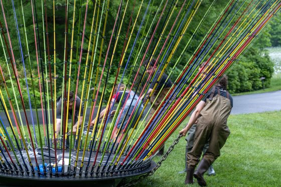 people moving a sculpture of real fishing rods onto a lake