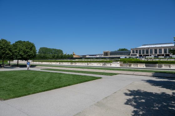 a person walking across a small grass lawn in the foreground with a large Conservatory in the background