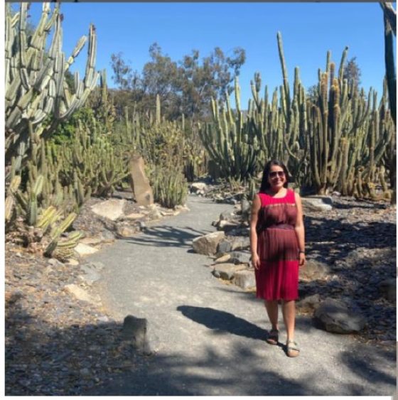 woman in a red dress standing in front of tall plantings of cacti