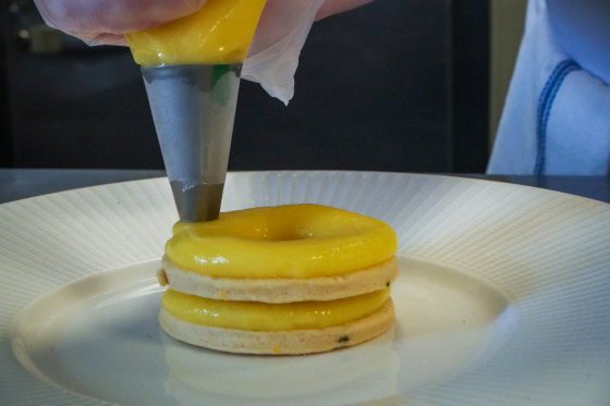someone piping lemon curd onto two stacked circle cookies