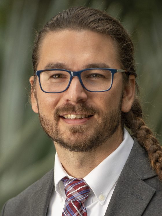 person in a gray suit with blue glasses looking at the camera