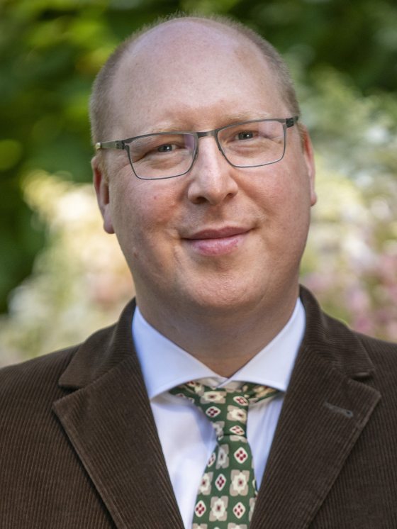 person in a brown suit with gray glasses looking at the camera