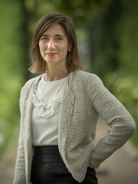 person with green and white fringed knit sweater over a ruffled white top smiles at the camera