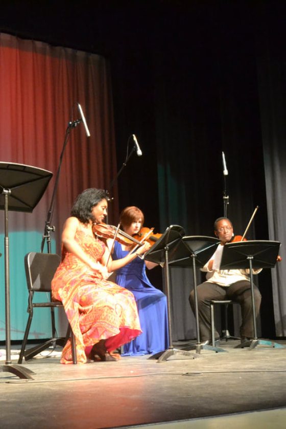 3 musicians seated on stage playing violins