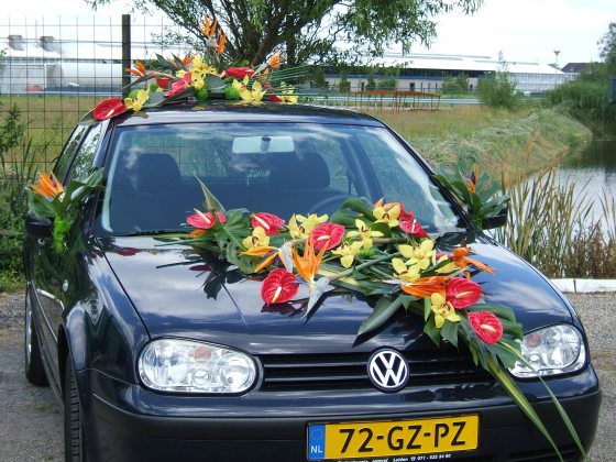 a black VW car decorate with red, yellow, and orange flowers on top of the rood and hood