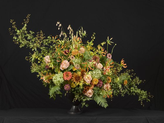 a geometric floral arrangment design of a variety of flowers including mums and roses - all shaped like a diamond in a black vase with black background