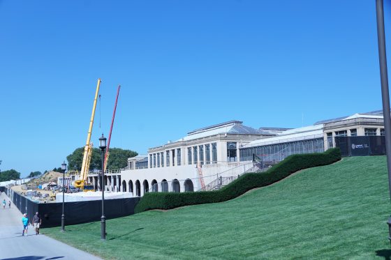 green grass in the foreground with two large cranes working on a building on the left