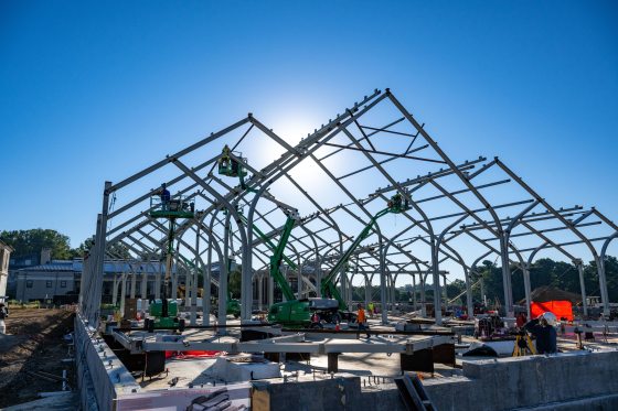 steel beams being placed with green cranes to form a large structure