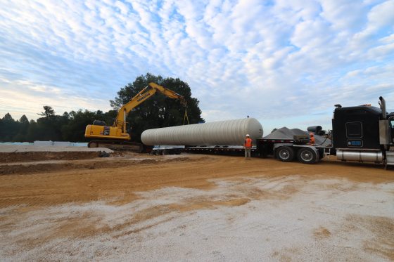 a yellow crane unloading a large white tank off of a tractor trailer