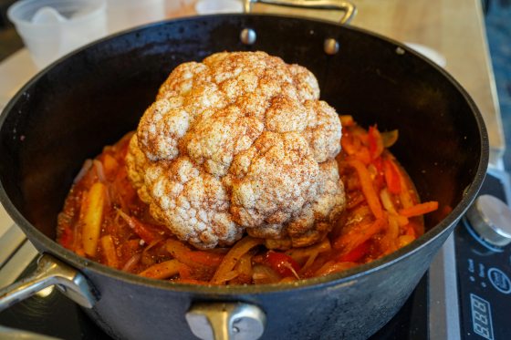 a head of cauliflower sitting in a pot of sliced peppers