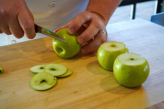 a person slicing three green apples on a wood cutting board
