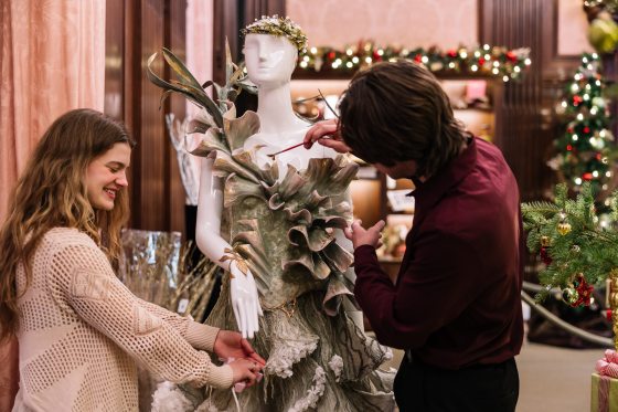 two people adjusting a green dress made of floral material