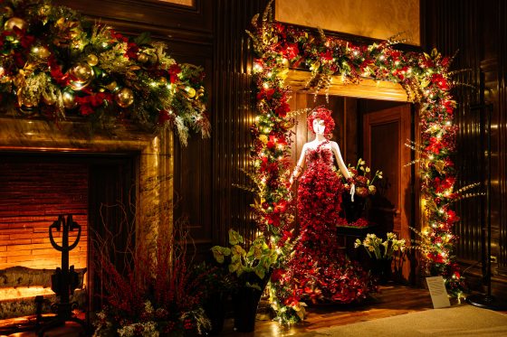 a mannequin in a dress made of red floral material placed in an alcove with christmas garland around it