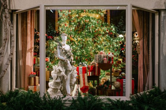 a green dress made of floral material on a white mannequin standing in front of a christmas tree