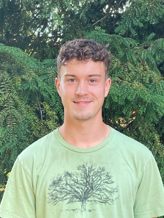 portrait of smiling person with short brown hair and green t-shirt with the sketch of a tree