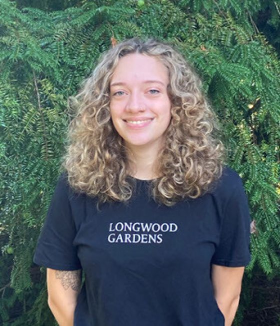 portrait of smiling person with long curly blonde hair and a navy Longwood Gardens t-shirt