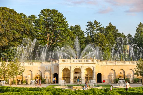 Fountains shoot up in arched forms over a white stone facade in a garden during the day
