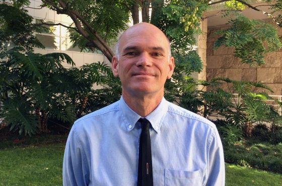 a person in a blue shirt and black tie looking directly at the camera