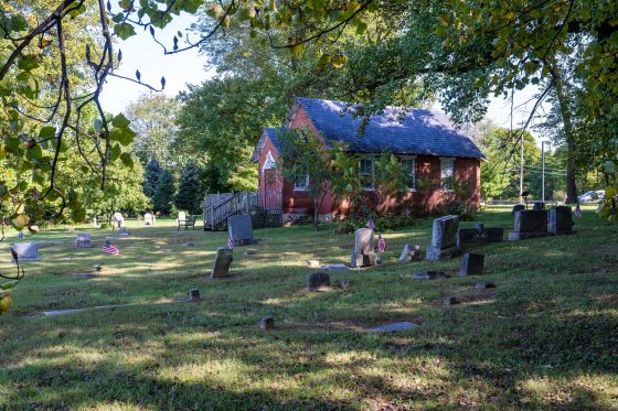a red brick meeting house with blue roof and cemetery stones in the front