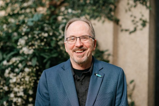 a person in a blue blazer and black shirt smiling at the camera