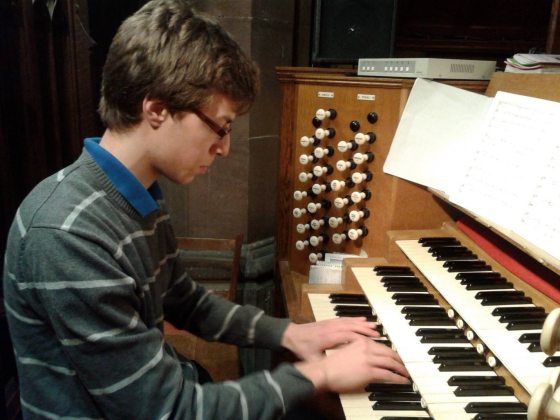 a person in a striped shirt and glasses playing an organ