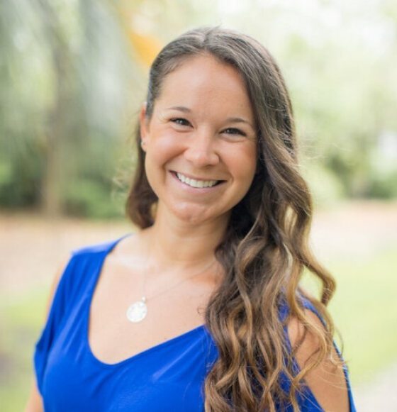 A woman in a blue shirt with curly brown hair smiles for a photo