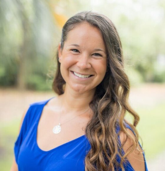 A woman in a blue shirt with curly brown hair smiles for a photo 