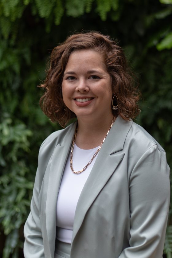 Abby Lorenz poses next to Longwood's Green Wall in a grey suit.