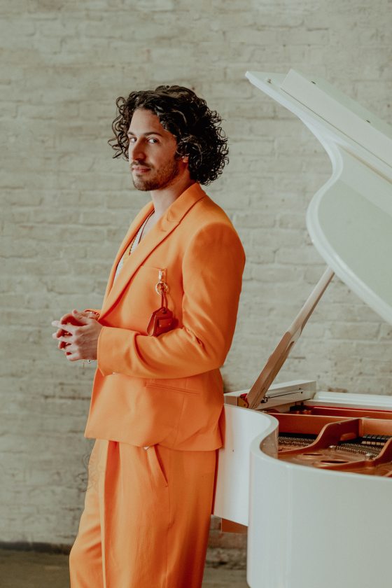 Musician posing against an open white piano