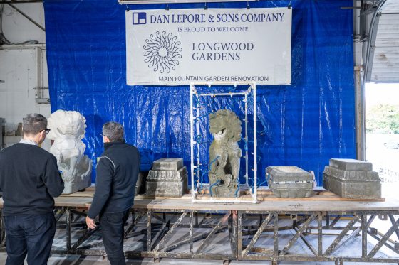 two people standing at a work table examining stone sculptures