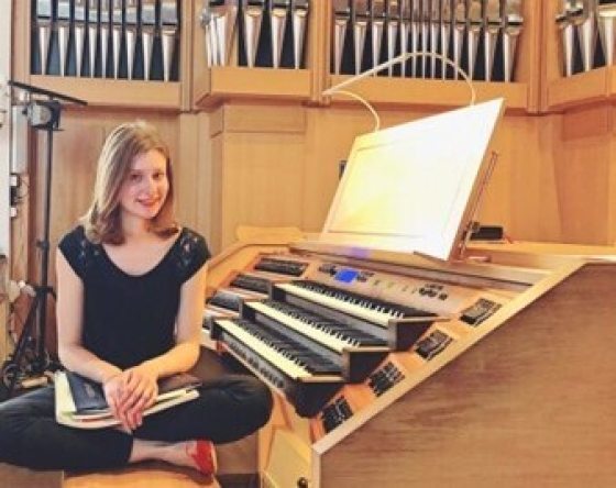 a teenager in a black outfit sitting at an organ smiling at the camera