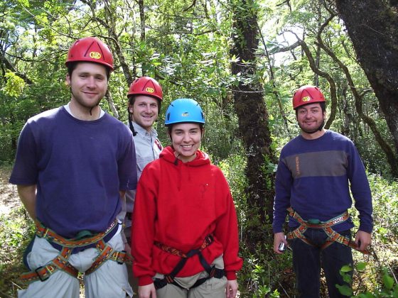 A group of four people in safety helmets and climbing harnesses smiling at the camera.