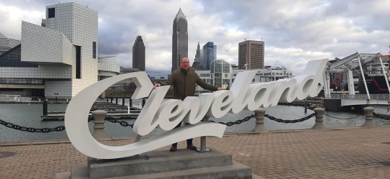 A person standing behind a sign that says Cleveland, along a large river.