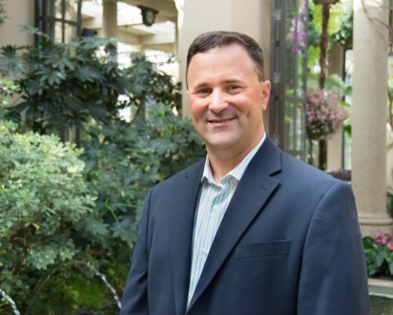 A headshot of a person smiling at the camera in a blue shirt and blazer. 