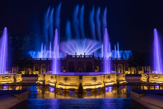 Illuminated fountains in shades of purple shooting up in the air in a variety of designs. 