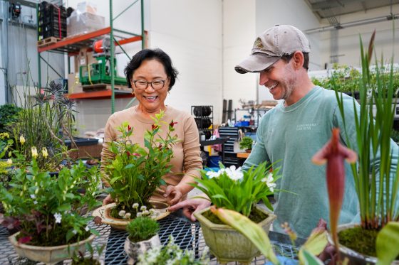 Two people standing at a table looking at plants and smiling.