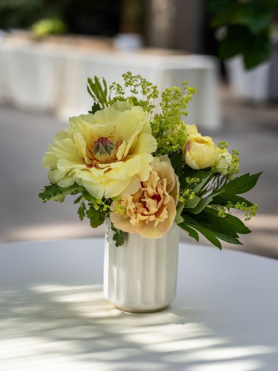 A white vase filled with yellow flowers on a white tablecloth.