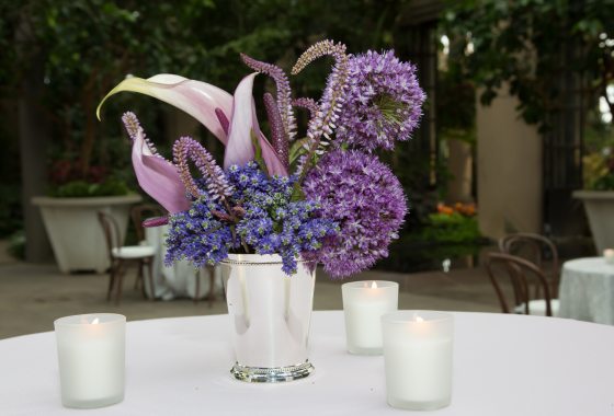 A silver vase filled with purple blooming flowers on a white tablecloth.