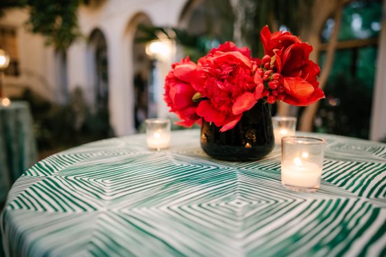 A black vase filled with red flowers on a geometric patterned tablecloth.